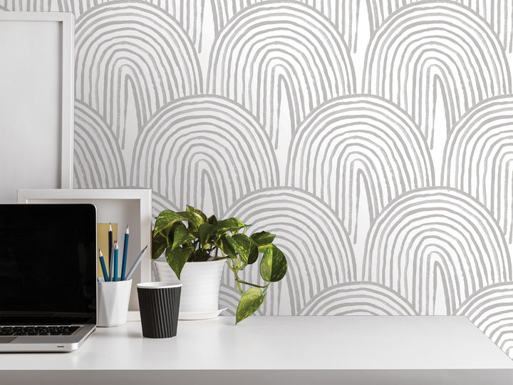 a white desk with various items on it, including a laptop, a plant, a cup, and a framed picture. The background has a repeating pattern of white and gray arches, creating a minimalist and modern aesthetic.