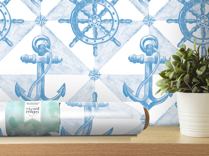 a wallpapered wall with a repeating pattern of blue anchors and a ship's wheel, along with a potted plant and a roll of wallpaper on a shelf.