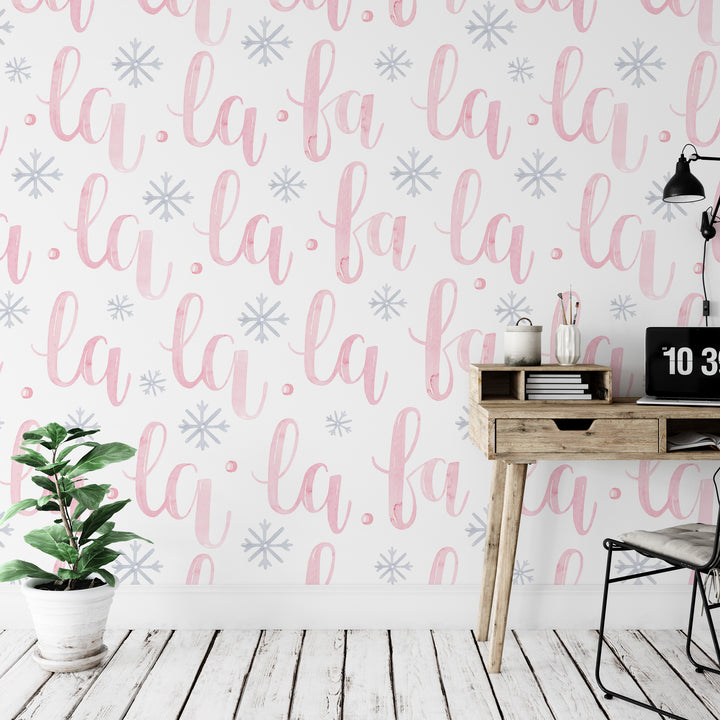 a wall with a repeating pattern of the word "la" in pink and white cursive font, along with snowflake-like designs. There is a wooden desk with a laptop and a plant on it, and a chair is positioned next to the desk.