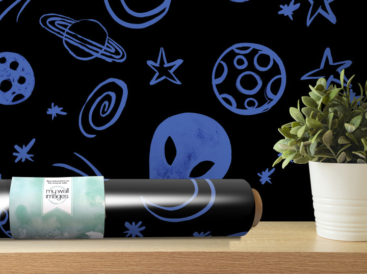 a black roller with a blue alien face design on it, placed on a wooden shelf next to a potted plant.