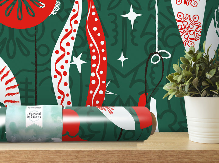 a roll of patterned wallpaper with a green and red design, placed on a wooden surface next to a potted plant.