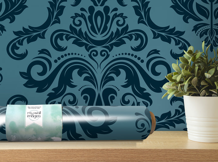 a roll of wallpaper with a blue and black damask pattern, placed on a shelf next to a potted plant.