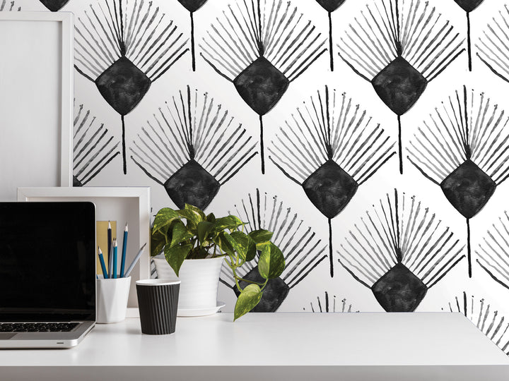 a white desk with various items on it, including a laptop, a plant, and some office supplies. The wall behind the desk has a repeating pattern of black and white geometric shapes, creating a visually striking backdrop.