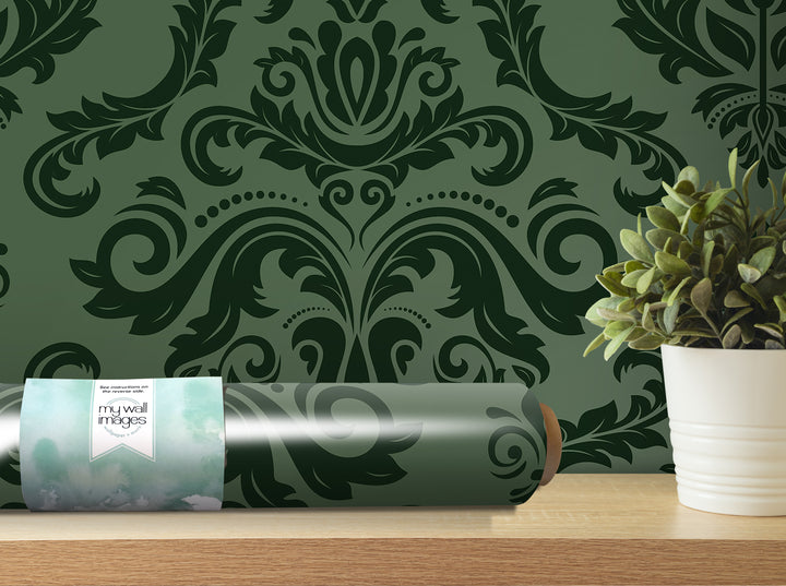 a roll of wallpaper with a green and black damask pattern, placed on a shelf next to a potted plant.