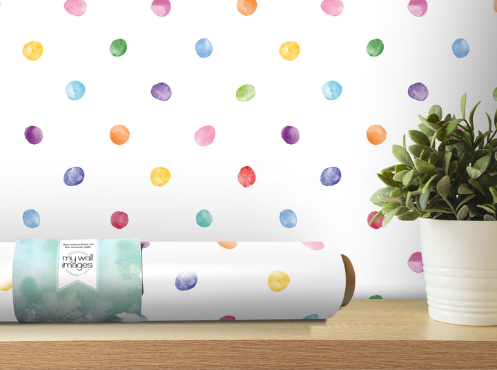 a colorful polka dot wallpaper on a wall, with a potted plant and a roll of wallpaper paper on a shelf in the foreground.