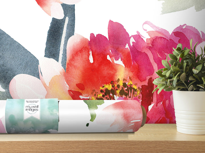 a large, vibrant watercolor painting of a flower on a wall, with a potted plant and a roll of wallpaper or paper with a floral design on a shelf in the foreground.