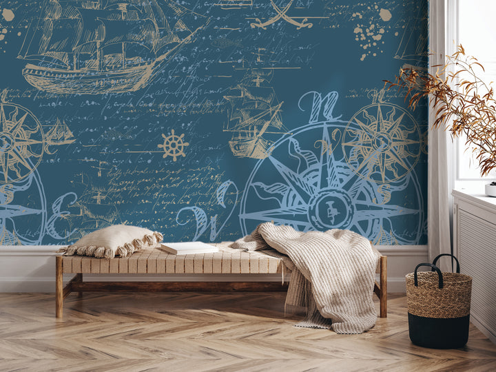 a room with a large blue wall mural depicting a nautical scene with ships, a compass, and other maritime elements. In the foreground, there is a wooden bench with a blanket draped over it, and a woven basket next to it.