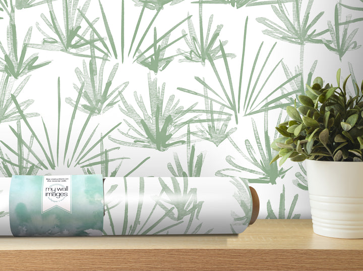 a roll of wallpaper with a green leaf pattern, placed on a wooden shelf next to a potted plant.