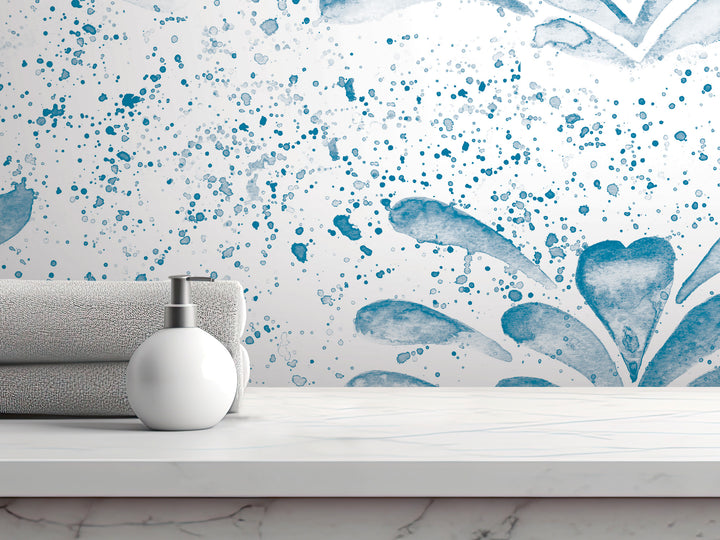 a white countertop with a white soap dispenser and a gray towel. The backdrop is a white wall with a blue watercolor-style design.