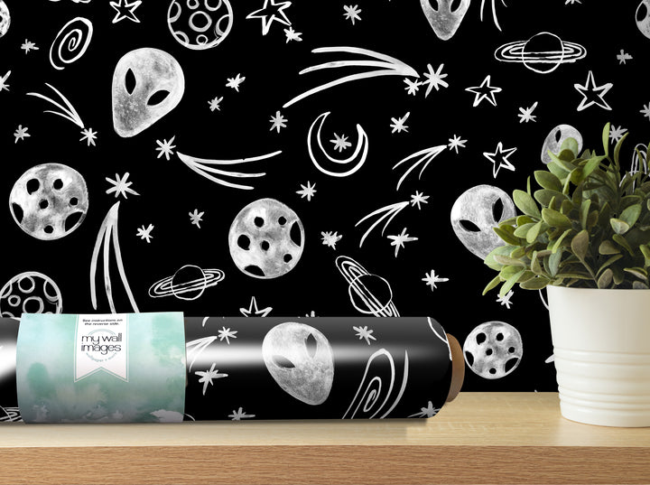 a black and white wallpaper with various celestial objects such as planets, stars, and comets, as well as a potted plant and a roll of wallpaper on a shelf.