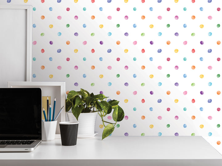 a white desk with a laptop, a plant, and various office supplies, including a cup and a pencil holder. The background has a colorful polka dot pattern, creating a playful and vibrant atmosphere.