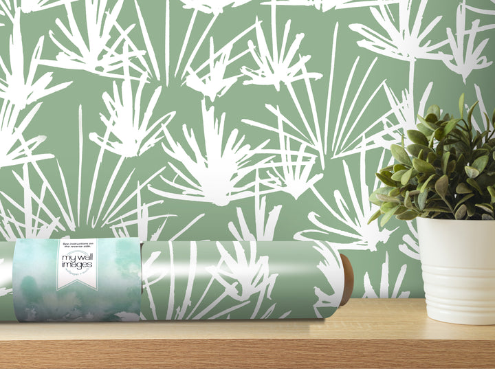 a roll of wallpaper with a white and green leafy pattern, placed on a wooden shelf next to a potted plant.