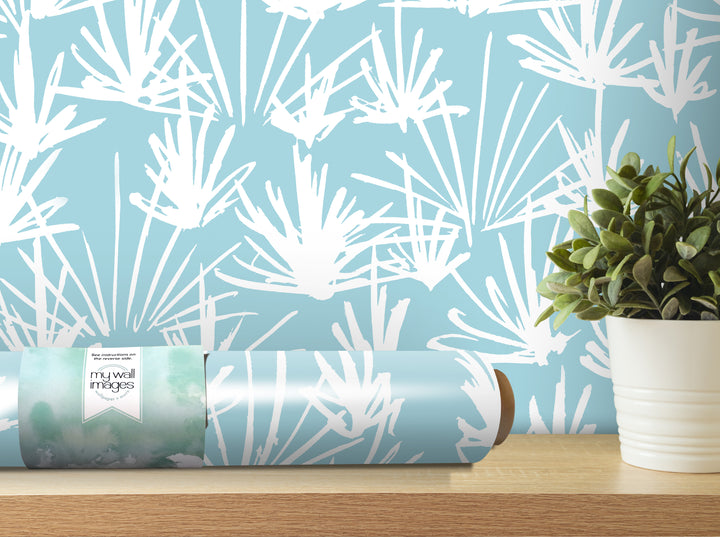 a roll of wallpaper with a white and blue abstract pattern, placed on a wooden shelf next to a potted plant.