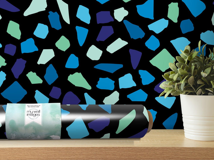 a vase with a plant on a table next to a roll of wrapping paper