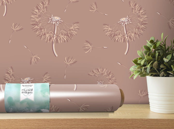 a pink wall with a dandelion pattern, a potted plant, and a roll of wallpaper with a dandelion design.