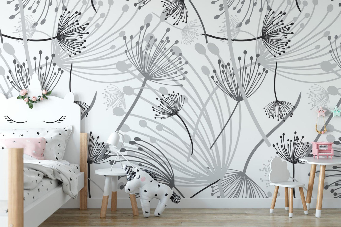 a child's bedroom with a white bed, a small table, and a chair. The walls are decorated with a black and white floral pattern, and there are two small stuffed animals in the room.