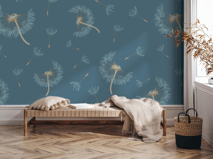 a cozy living room with a blue wall adorned with a repeating pattern of dandelions. In the center of the room, there is a wooden bench with a white pillow on it. To the right of the bench, there is a woven basket. A potted plant is also present in the room, adding a touch of greenery to the space.