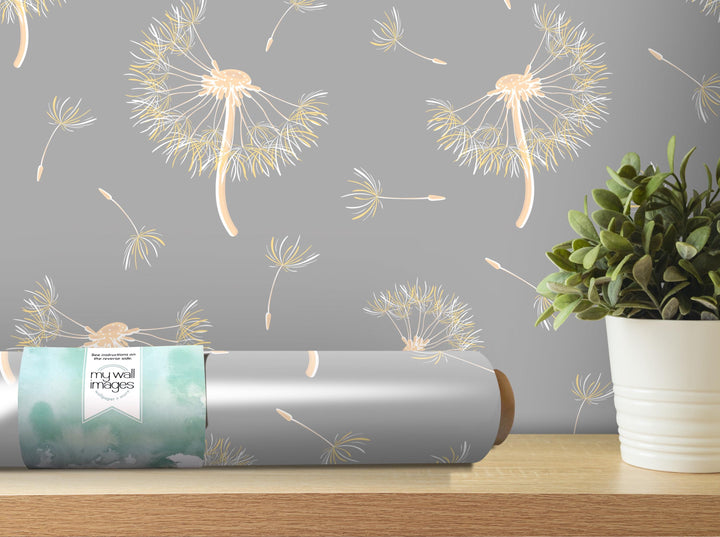a gray wall with a repeating pattern of dandelion-like designs in shades of yellow and white. A roll of wallpaper with a similar pattern is placed on a wooden shelf next to a potted plant.