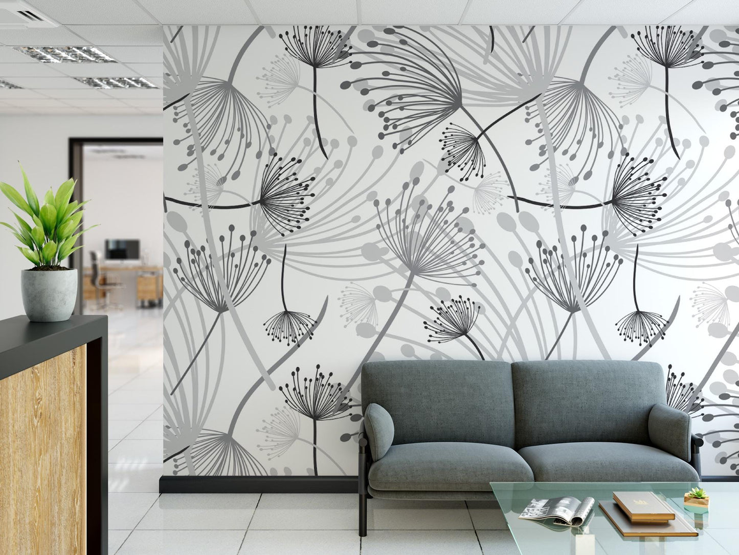 a modern office space with a gray sofa and a glass coffee table in the foreground. The wall behind the sofa is decorated with a repeating pattern of black and white dandelion-like designs. The office appears to be well-lit and clean, with a potted plant and a magazine on the coffee table adding to the contemporary aesthetic.