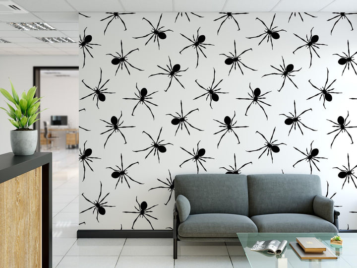 a modern office space with a gray sofa and a glass coffee table in the foreground. The wall behind the sofa is decorated with a repeating pattern of black spider silhouettes, creating a bold and striking visual effect.