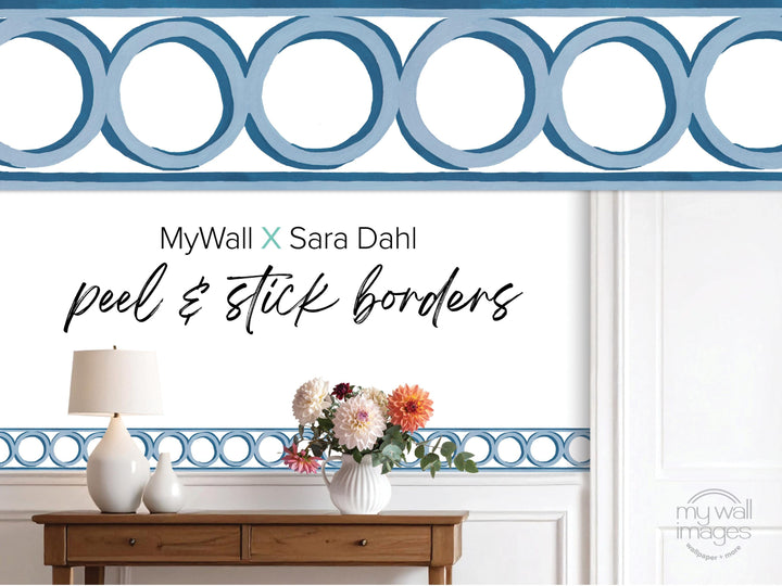 a wooden table with a vase of flowers, a lamp, and a blue and white geometric border design on the wall behind it.