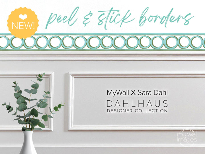 a white wall with a decorative border, a vase of greenery, and text that reads "MyWall X Sara Dahl Dahlhaus Designer Collection".