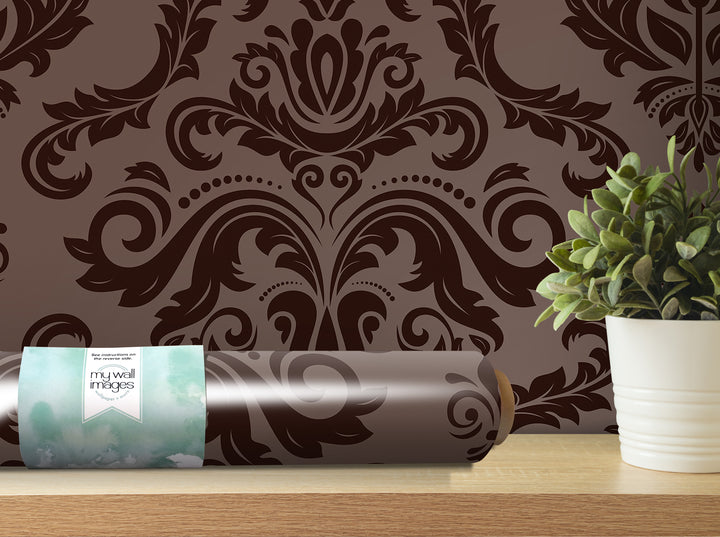 a brown and black damask wallpaper with a decorative pattern, a roll of wallpaper, and a potted plant on a shelf.