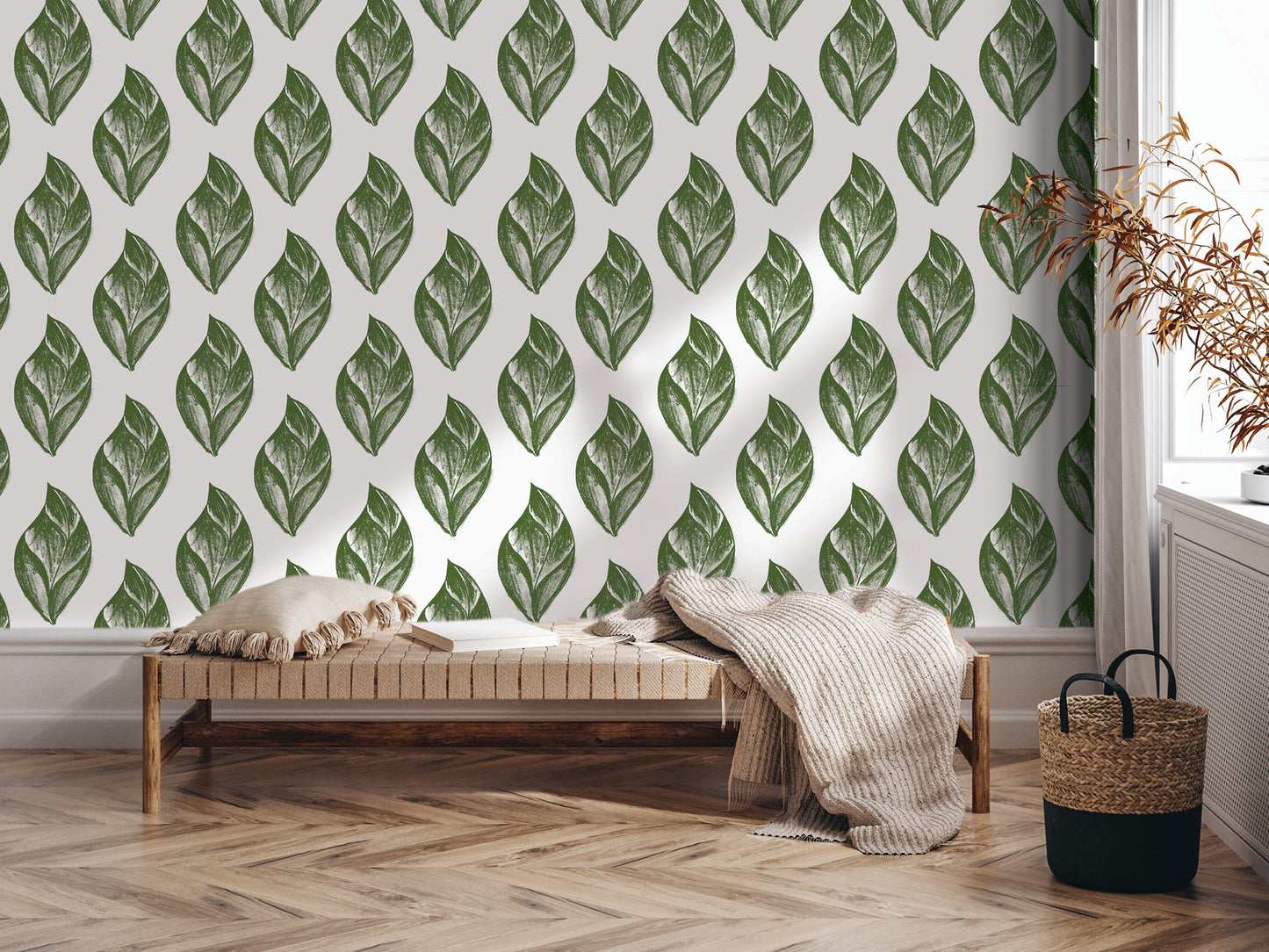 a modern living room with a wooden floor and a white wall adorned with a repeating pattern of green leaf designs. In the foreground, there is a wooden bench with a beige blanket draped over it, and a woven basket next to it.