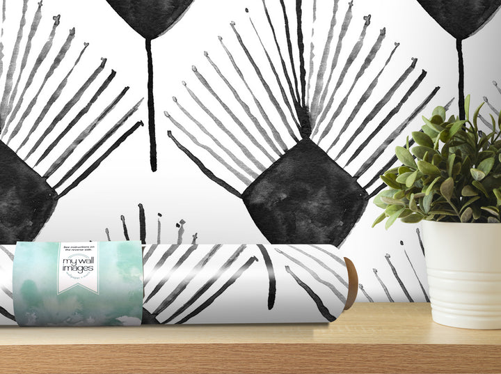 a black and white abstract pattern on a wall, with a potted plant and a roll of wallpaper on a shelf in the foreground.