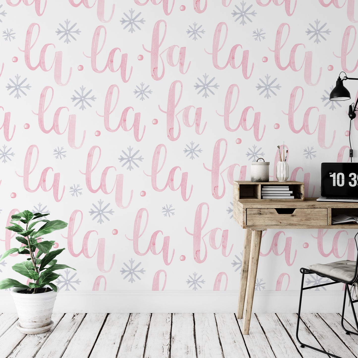 a wall with a repeating pattern of the word "la" in pink and white cursive font, along with snowflake-like designs. There is a wooden desk with a laptop and a plant on it, and a chair is positioned next to the desk.