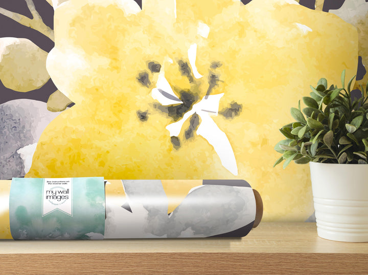 a roll of wallpaper with a yellow flower design, placed on a wooden surface next to a potted plant.