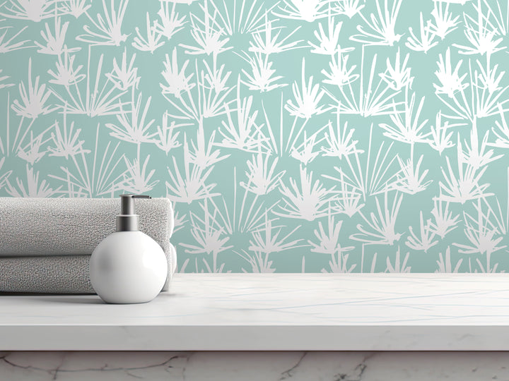 a white pump soap bottle on a white countertop, with a rolled-up gray towel underneath it. The backdrop is a wall with a repeating pattern of white and green leaves or flowers.