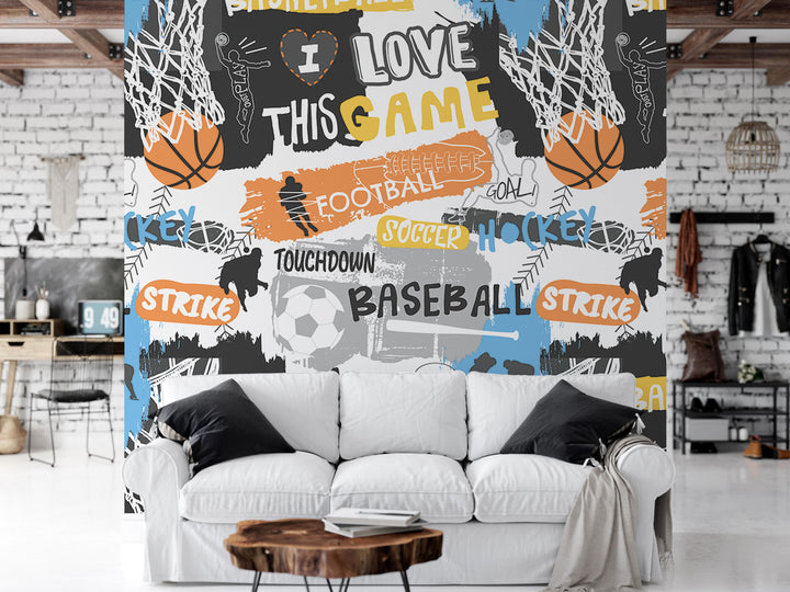 a vibrant and colorful wall mural with various sports-related elements, including basketballs, soccer balls, and baseball bats. The wall is adorned with the words "LOVE THIS GAME" and "TOUGH" prominently displayed, along with other sports-related phrases such as "TOUCHDOWN", "BASEBALL", and "STRIKE". In the foreground, there is a white couch with a wooden coffee table in front of it, creating a cozy and inviting atmosphere in the room.