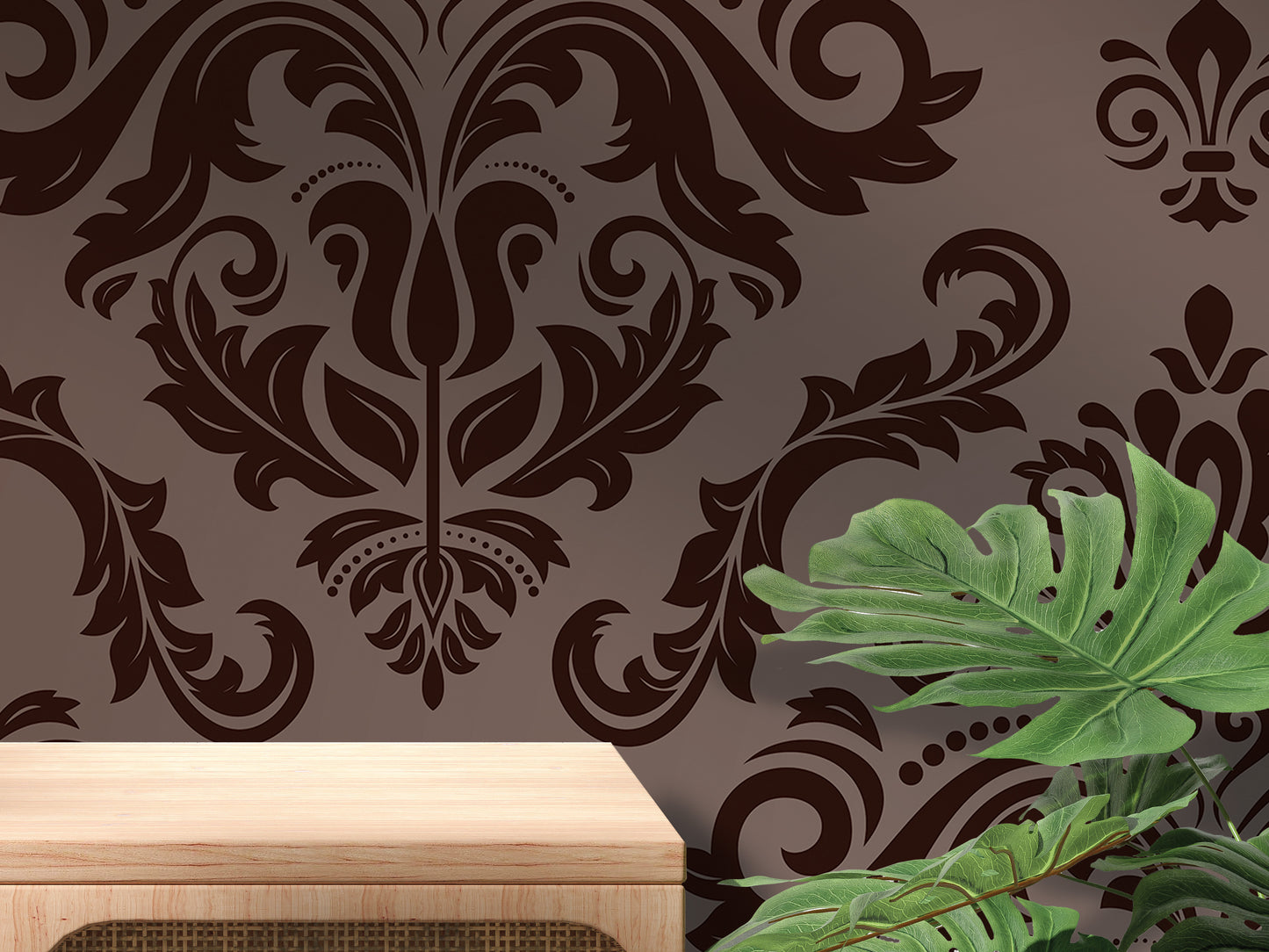 a dark brown damask pattern on a wall, with a wooden table in the foreground and a large green leaf plant in the background.