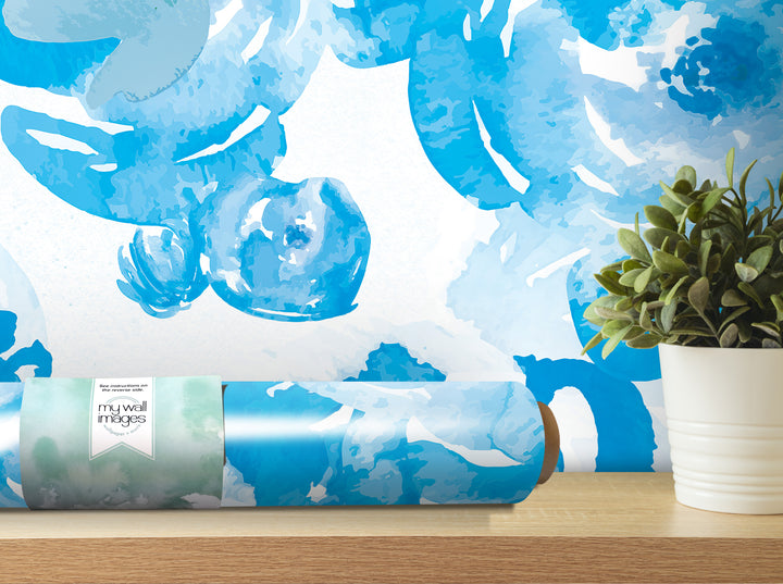 a blue and white floral wallpaper on the wall, with a potted plant and a roll of wallpaper on a shelf in the foreground.