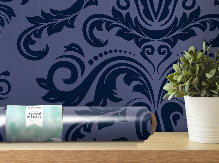 a roll of wallpaper with a blue and black damask pattern, placed on a shelf next to a potted plant.