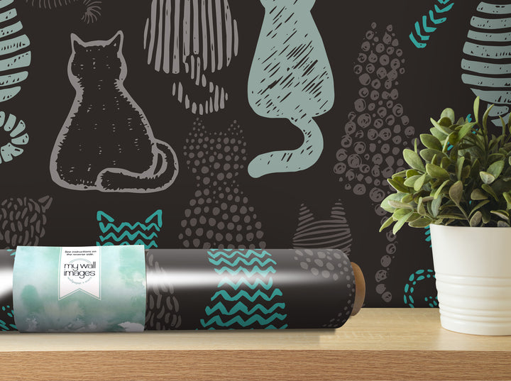 a black and teal cat wallpaper roll placed on a wooden shelf next to a potted plant.