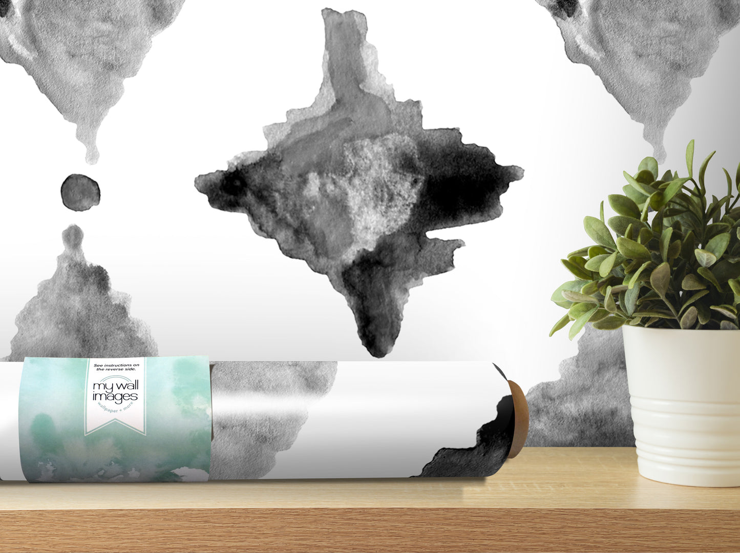 a roll of wallpaper with a black and white abstract design, placed on a wooden shelf next to a potted plant.