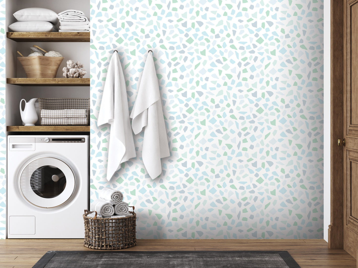 a bathroom with a tiled wall featuring a mosaic pattern in shades of blue and green. The bathroom is equipped with a washing machine and a wooden shelf with various items, including towels and baskets.