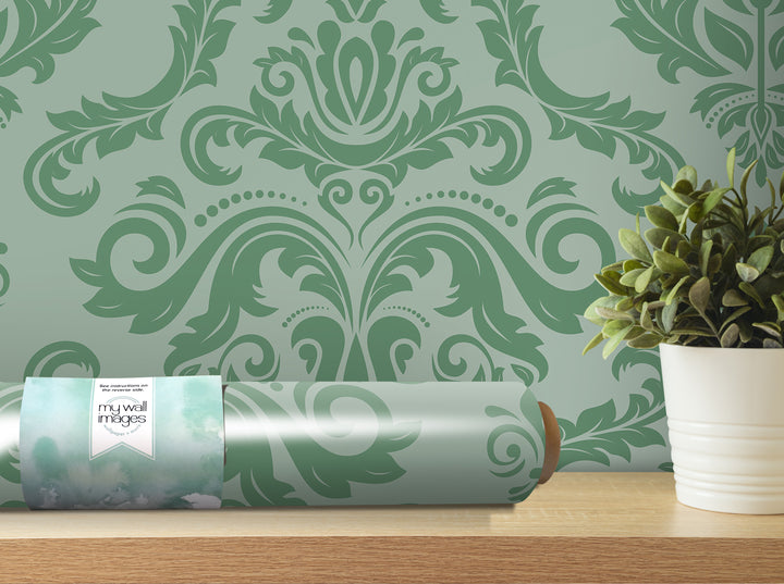 a decorative green and white wallpaper with an ornate floral pattern, a potted plant, and a roll of wallpaper on a shelf.