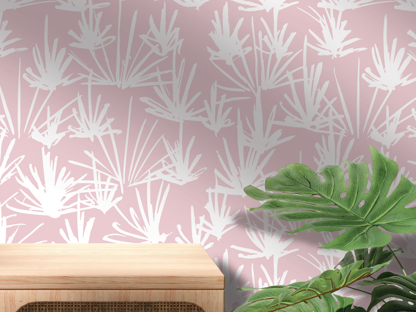 a pink wall with a white leaf pattern, a wooden table, and a large green leaf plant.