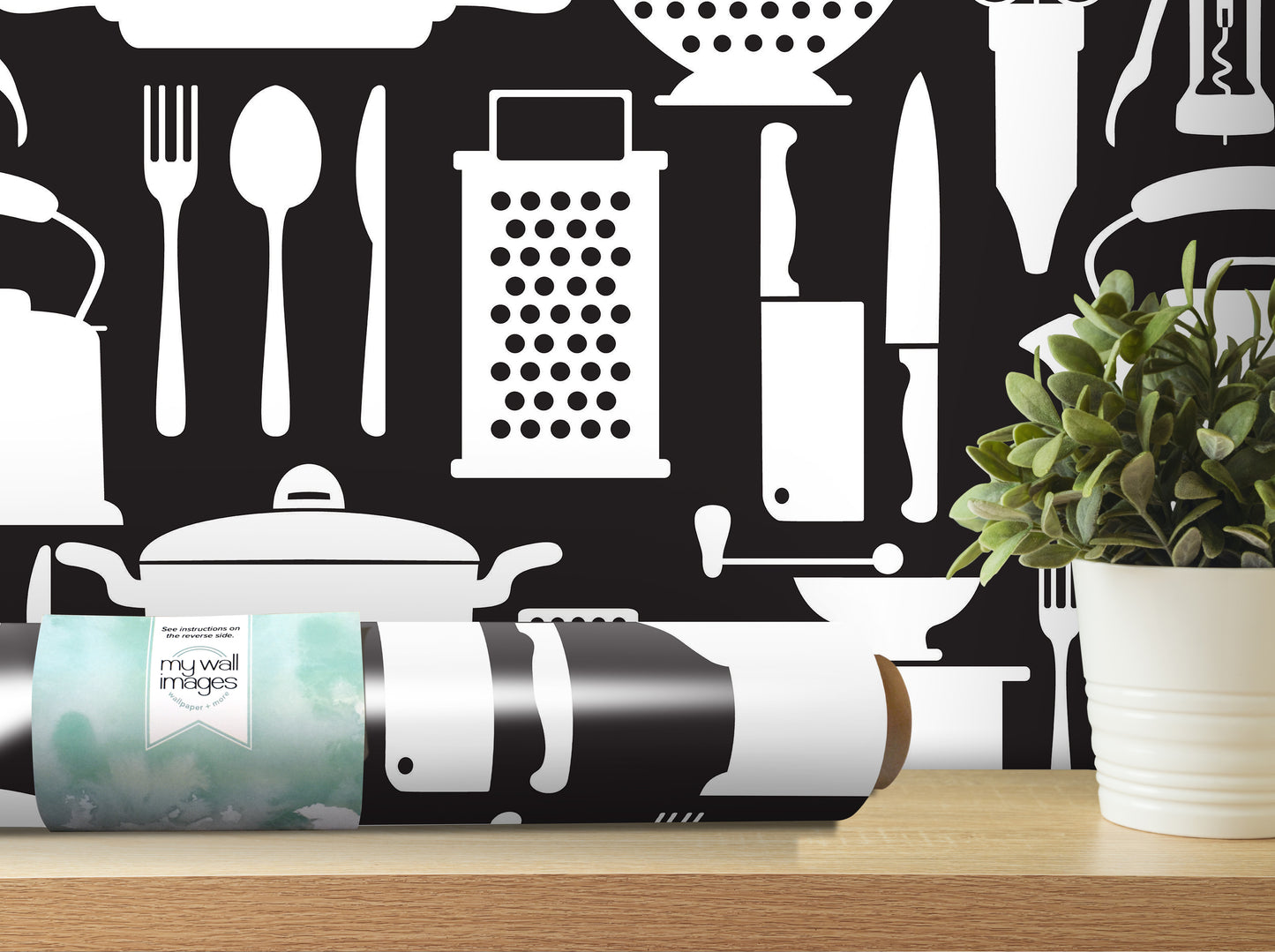 a black and white wallpaper with various kitchen utensils and appliances, such as a knife, a grater, a pot, and a teapot, as well as a potted plant. The wallpaper is displayed on a wall, and there is a roll of wallpaper paper on a table in front of it.