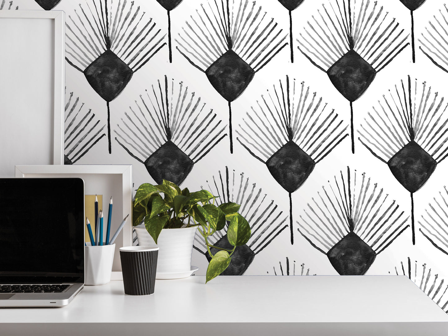a white desk with various items on it, including a laptop, a plant, and some office supplies. The wall behind the desk has a repeating pattern of black and white geometric shapes, creating a visually striking backdrop.