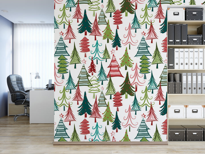a wall with a repeating pattern of Christmas trees in various colors, including red, green, and white. The wall is decorated with a festive design, creating a warm and cheerful atmosphere. In the background, there is a desk with a computer and a bookshelf filled with books and binders.