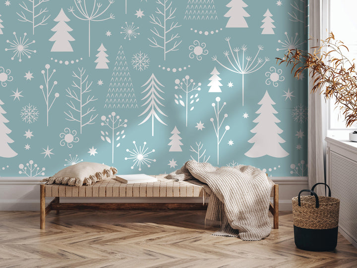 a cozy and inviting living space with a wooden floor and a comfortable bench. The wall behind the bench is decorated with a pattern of white trees and snowflakes, creating a wintery atmosphere. A woven basket is placed next to the bench, and a potted plant is located nearby. The overall scene conveys a sense of warmth and tranquility, with the natural elements complementing the comfortable furnishings.