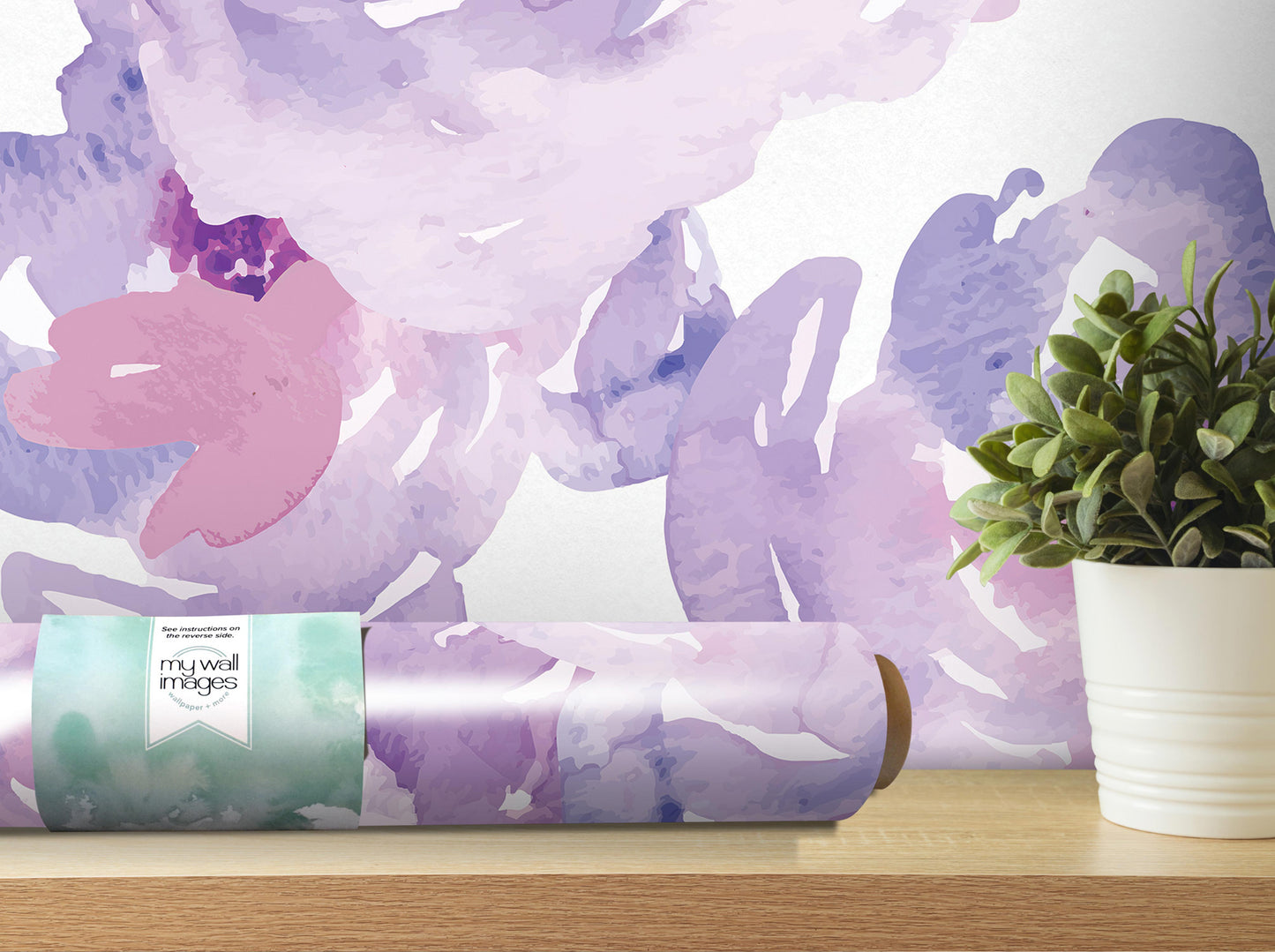 a roll of wallpaper with a watercolor-style design, placed on a wooden shelf next to a potted plant.