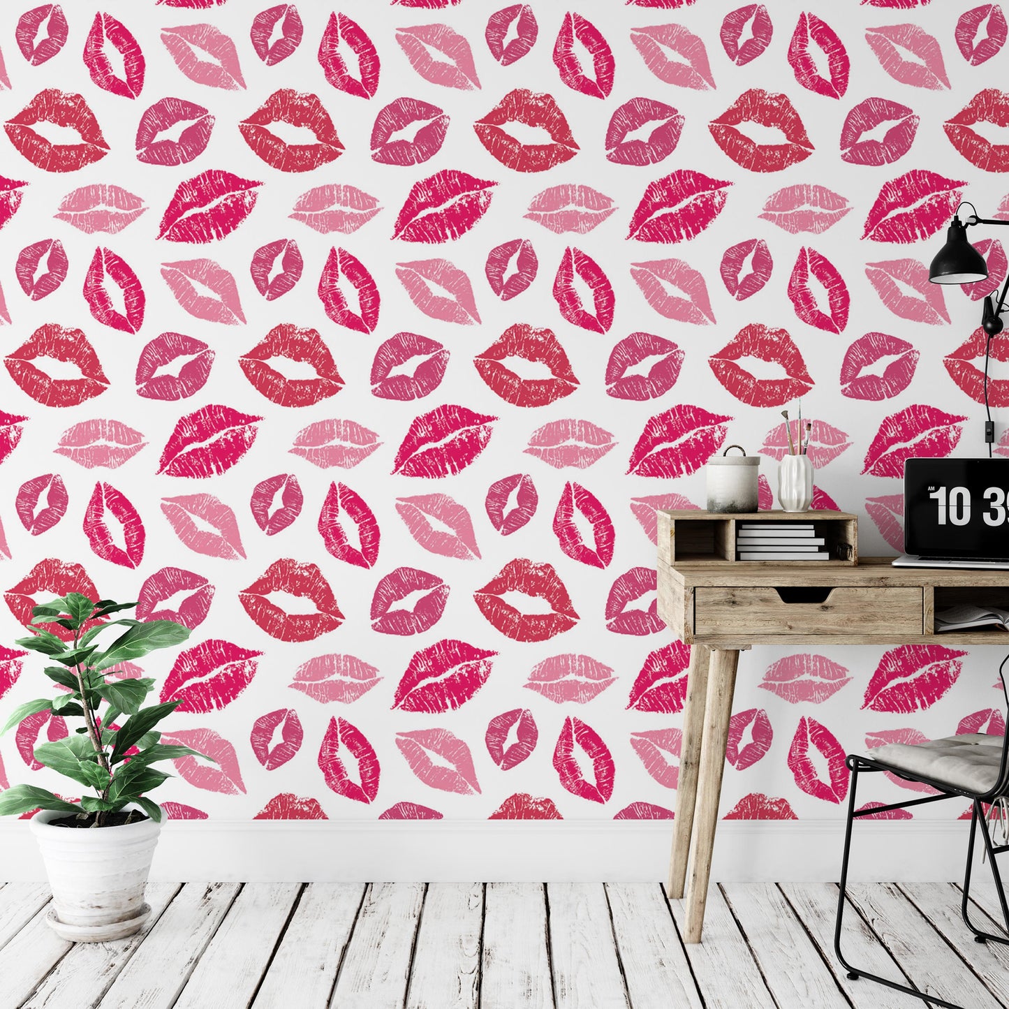 a wallpapered wall with a repeating pattern of red lips on a white background. There is a wooden desk with a laptop and a plant on it, and a black chair is positioned next to the desk.