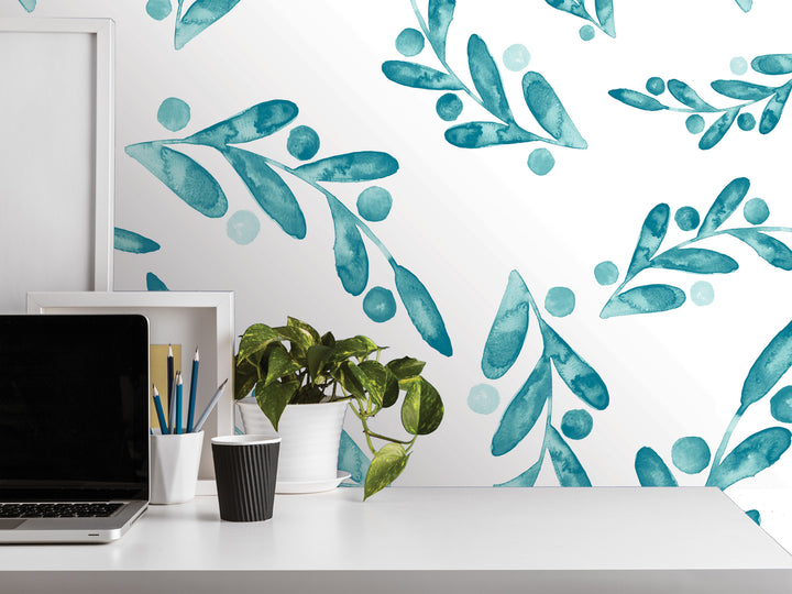 a white desk with a laptop, a plant, and various office supplies, including a cup and a pencil holder. The desk is set against a wall with a repeating pattern of blue and green watercolor leaves and circles, creating a calming and natural atmosphere.