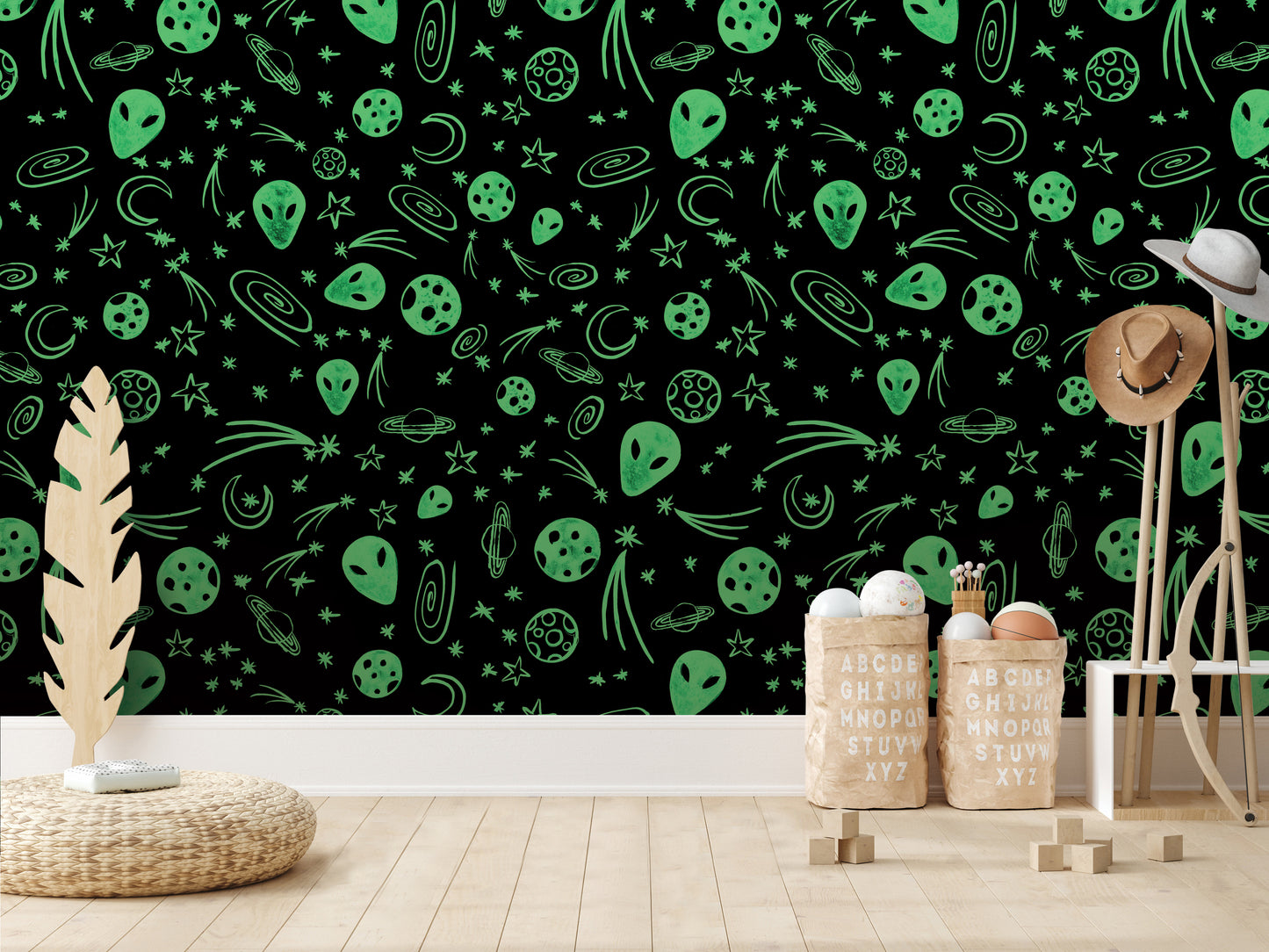 a wallpapered wall with a black background adorned with various green alien and celestial motifs, such as planets, stars, and comets. In the foreground, there are two wooden stools and a woven basket, and a wooden structure with a hat on top.