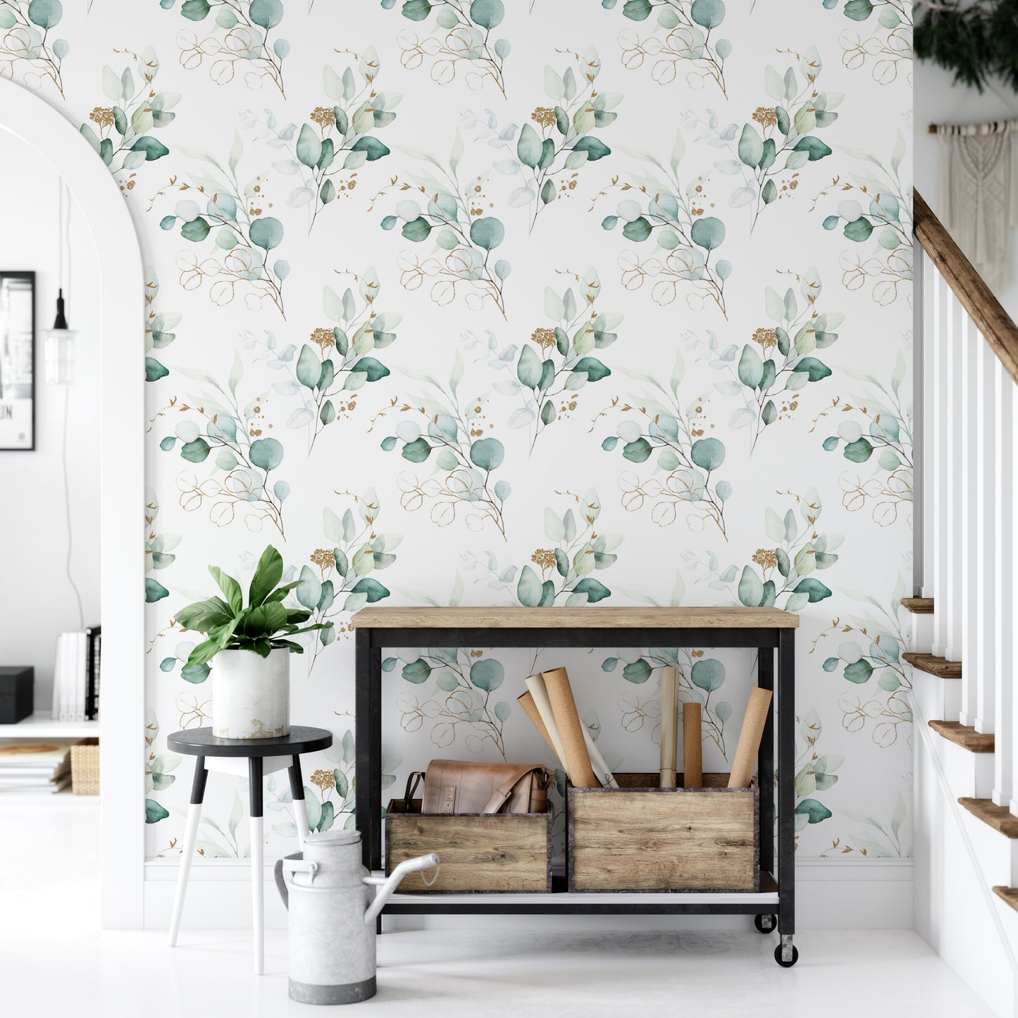 a modern and minimalist interior design with a white wall adorned with a repeating pattern of green and gold leaves. In the foreground, there is a black metal table with a wooden shelf holding various items, including a potted plant, a white vase, and a wooden crate. The overall color scheme and arrangement of the objects create a cohesive and visually appealing space.